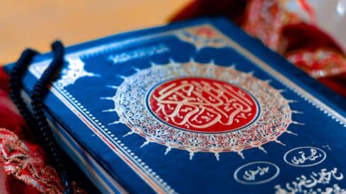 The image shows a Quran cover with ornate Arabic calligraphy and black prayer beads.