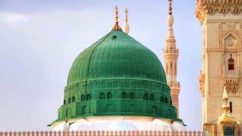 Large green dome prophet mosque with golden finials, mosque complex, adjacent minarets, beige stonework.