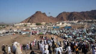 Large crowd in traditional attire at a colorful market, mountainous backdrop, arid region.