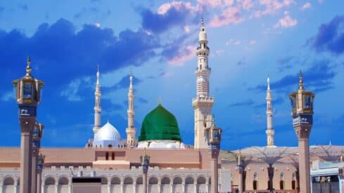 Mosqueof prophet with minarets, green and white domes, under blue sky with clouds, ornate lamp posts visible.