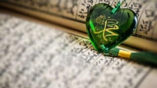 Heart-shaped green ornament with Arabic calligraphy on an open book, used as a bookmark.