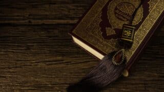 Ornately detailed book with gold accents on wood surface, decorative tassel beside it.