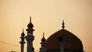 Silhouette of a mosque with minarets and dome at sunset.