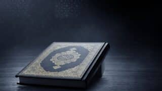 holy Quran with ornate Arabic calligraphy and gold patterns on dark surface in dim light.