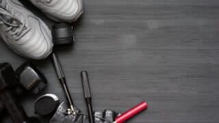 Fitness gear, including shoes, dumbbells, rope, gloves, on dark wooden surface, left side.