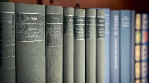 Row of green and blue hardcover books with titles on spines, arranged on a shelf.