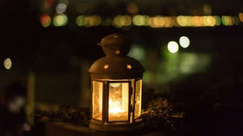 Lit lantern with star cutouts outdoors, warm glow, blurred background suggesting nighttime scene.