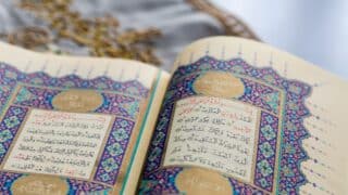 Open holy Quran page with ornate Arabic calligraphy and colorful decorative borders.