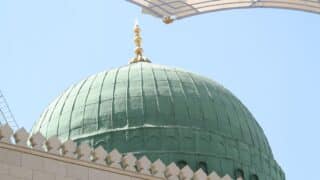 Prophet's Mosque dome with golden finial, clear blue sky background, decorative base elements visible.