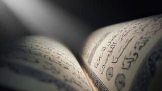 Open book in Arabic script with intricate calligraphy and soft light highlights.