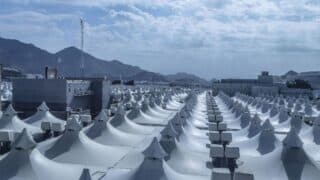 Array of white conical tents with mountains and structures in the background.