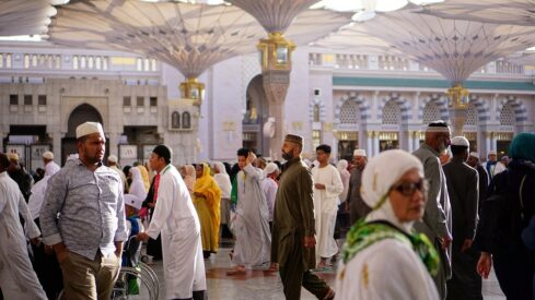 People in traditional attire walk in a courtyard under large decorative umbrellas.