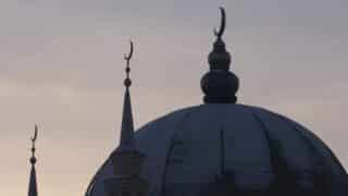 Mosque silhouette with dome and minarets against a dusky sky, featuring crescent moon finials.