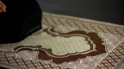 Prayer rug with intricate brown and cream patterns, dark fabric visible on one edge.