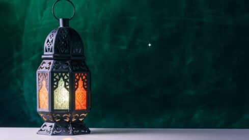 Decorative lantern with multicolored light on green background, small sparkle nearby.