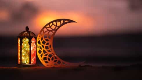 Decorative lantern with colorful glass beside crescent cutout at sunset, warm ambiance.