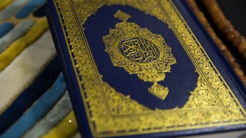 Richly decorated blue book cover with intricate gold Arabic designs on colorful fabric.