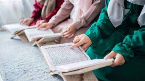 People reading Quran on wooden stands, wearing colorful traditional clothing and headscarves