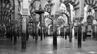 Interior space with striped arches, columns, tiled floor, and hanging lamps in symmetrical design.